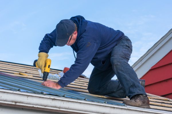 A man working on screwing in a tin roof on a house